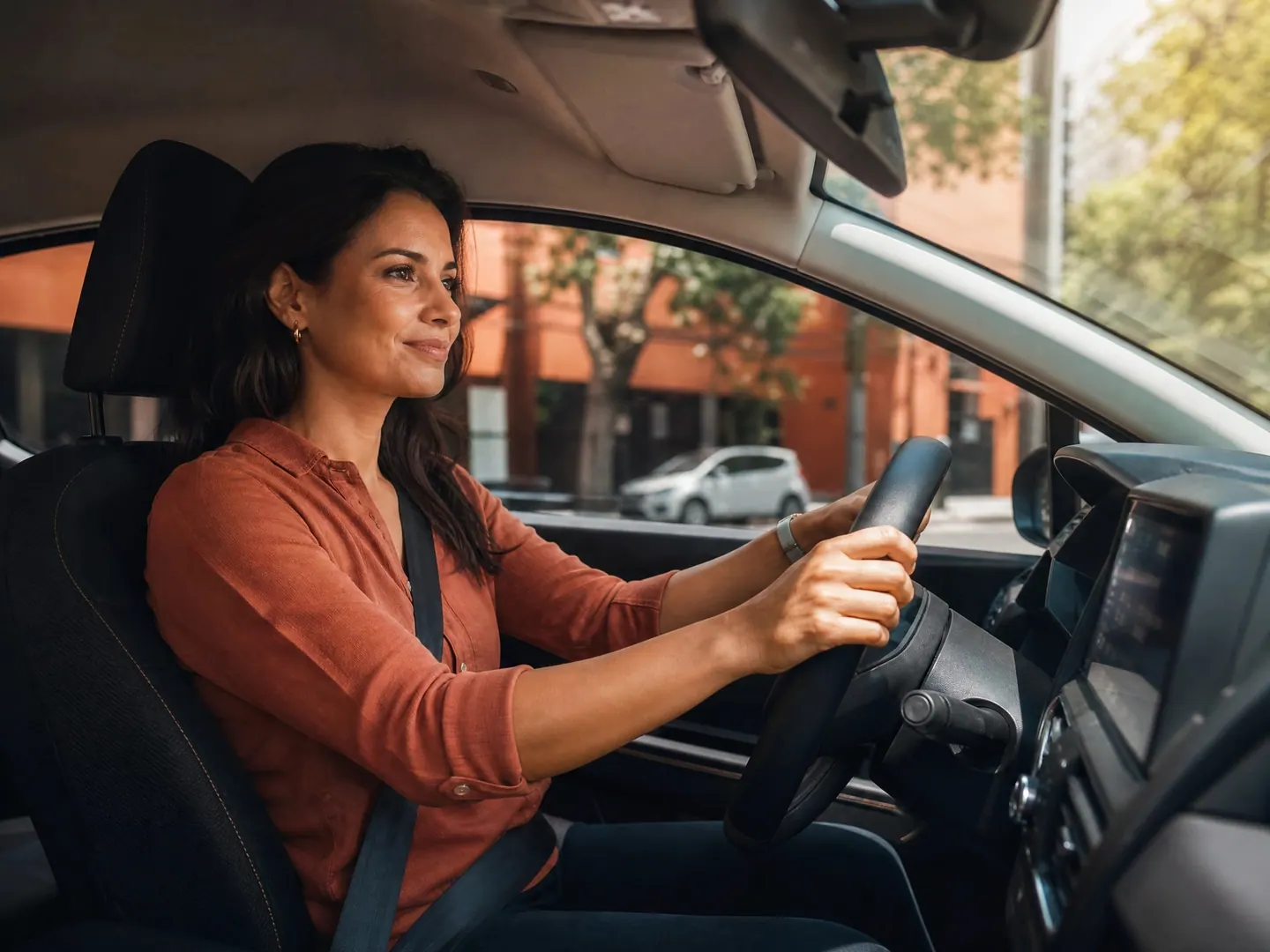 Mulher dirigindo o próprio carro pela cidade, com o cinto de segurança afivelado.